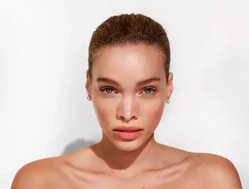 Une femme à la peau lisse et éclatante, avec des lèvres pulpeuses, fixe l’objectif avec assurance.